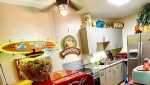 Una cocina con una máquina expendedora de Coca-Cola, un ventilador de techo y un refrigerador.