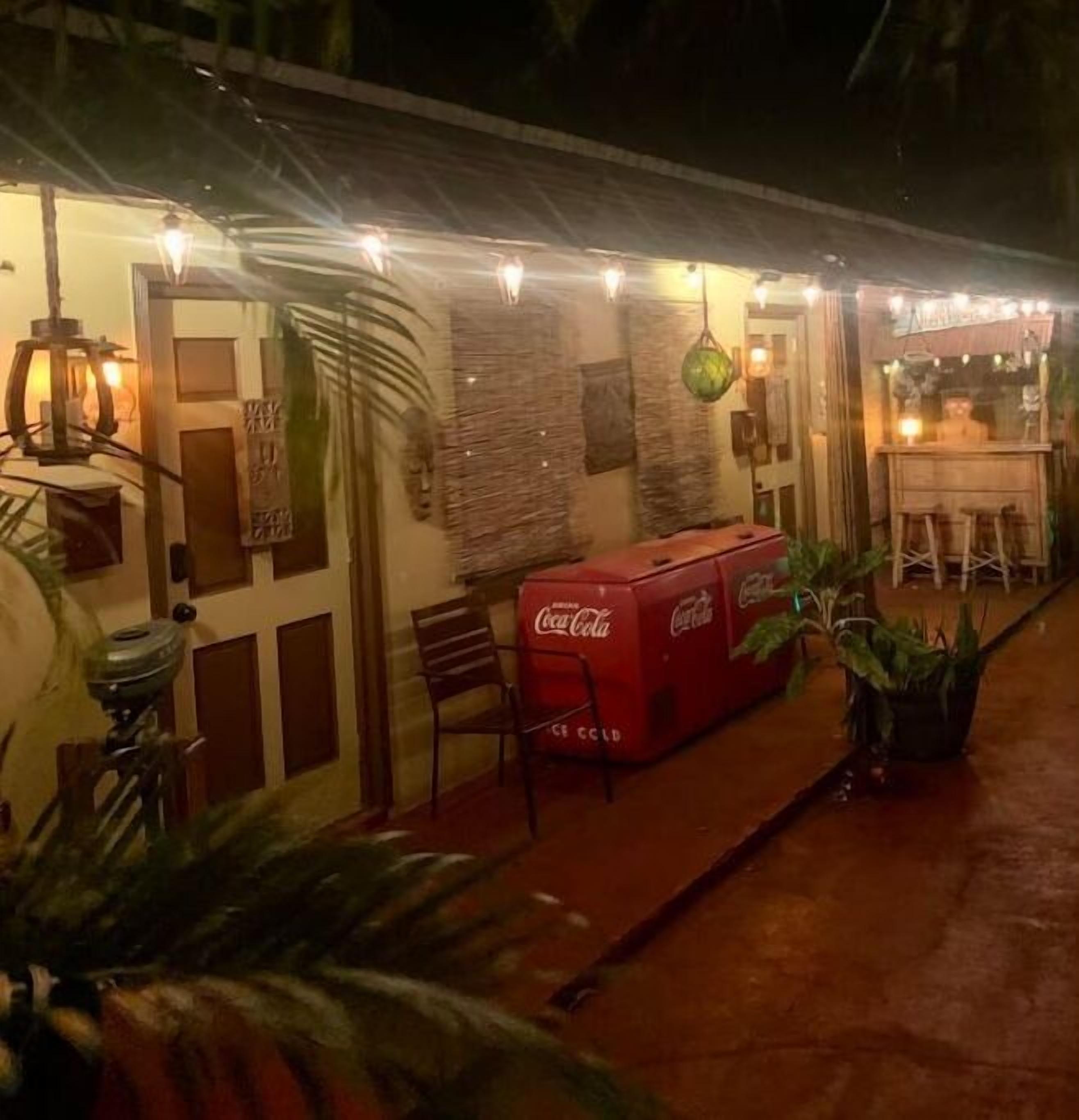 An outdoor seating area with a Coca-Cola cooler, chairs, and string lights.