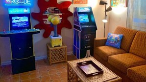 Una habitación con dos máquinas de arcade, un sofá, una lámpara y una mesita.