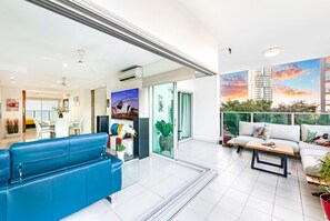 A modern living room with a blue sofa, a dining area, and a balcony with a cityscape mural.