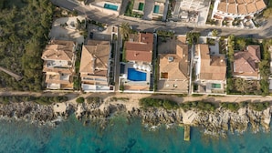 An aerial view of a coastal residential area with houses, a swimming pool, and rocky shoreline. - VILLA PRESIDENTE (Alcúdia)