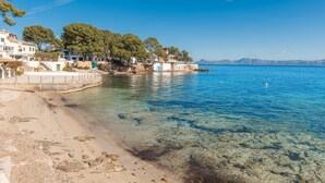 A coastal area with clear water, a sandy beach, and buildings along the shore. - VILLA PRESIDENTE (Alcúdia)