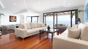 A modern living room with a large sofa, a glass coffee table, and a view of the sea. - VILLA PRESIDENTE (Alcúdia)