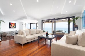 Ein modernes Wohnzimmer mit einer großen Couch, einem Glastisch und Meerblick durch große Fenster.