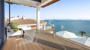 A balcony with a wooden floor, white furniture, and a view of the sea. - VILLA PRESIDENTE (Alcúdia)