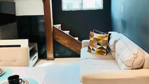 A modern living room with a staircase, a white sofa, and a patterned pillow. - Cobertura C/suíte - Salvador à 2km Praia Aeroporto (Centro Lauro de Freitas)