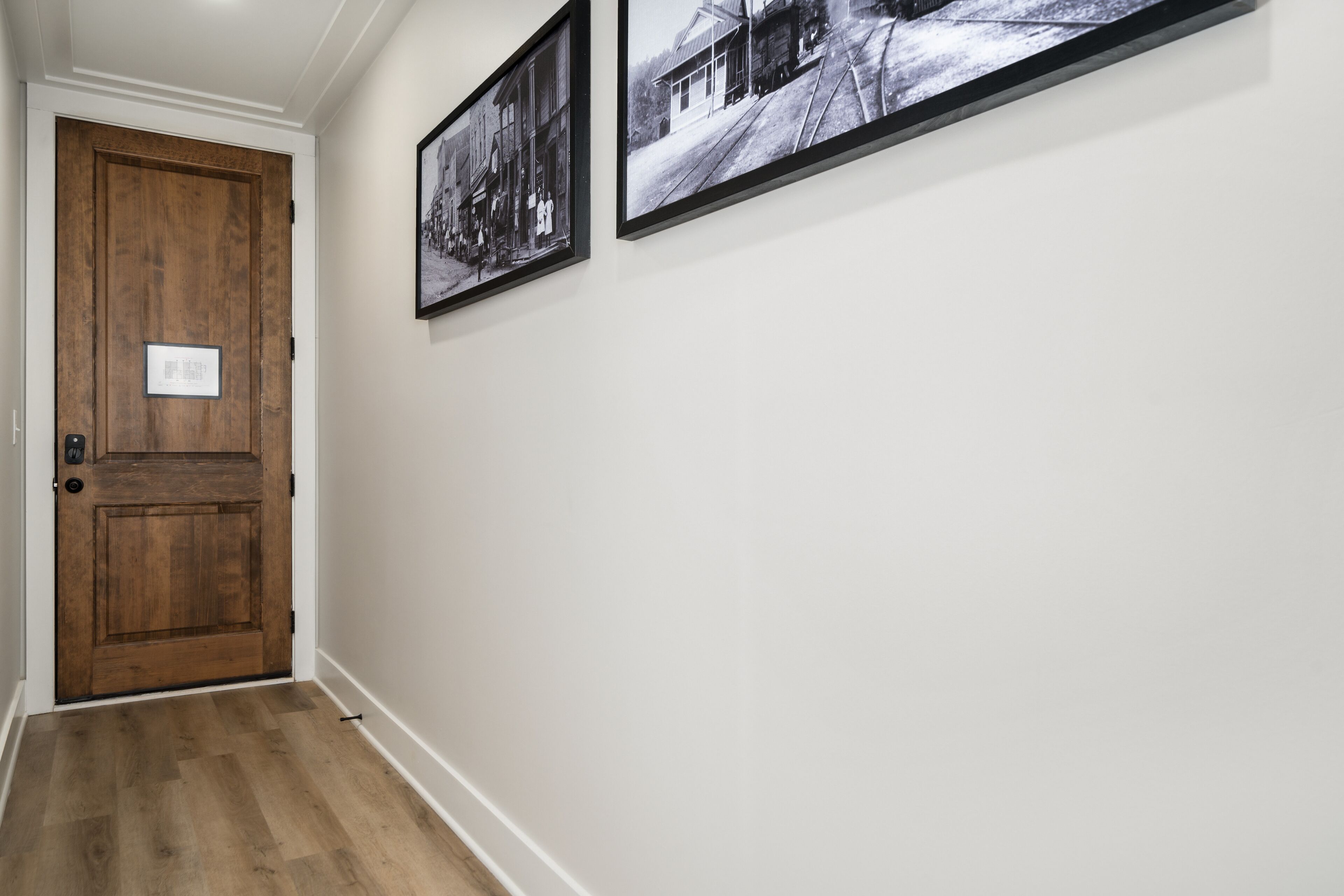 A hallway with a wooden door and two black and white photographs on the wall.