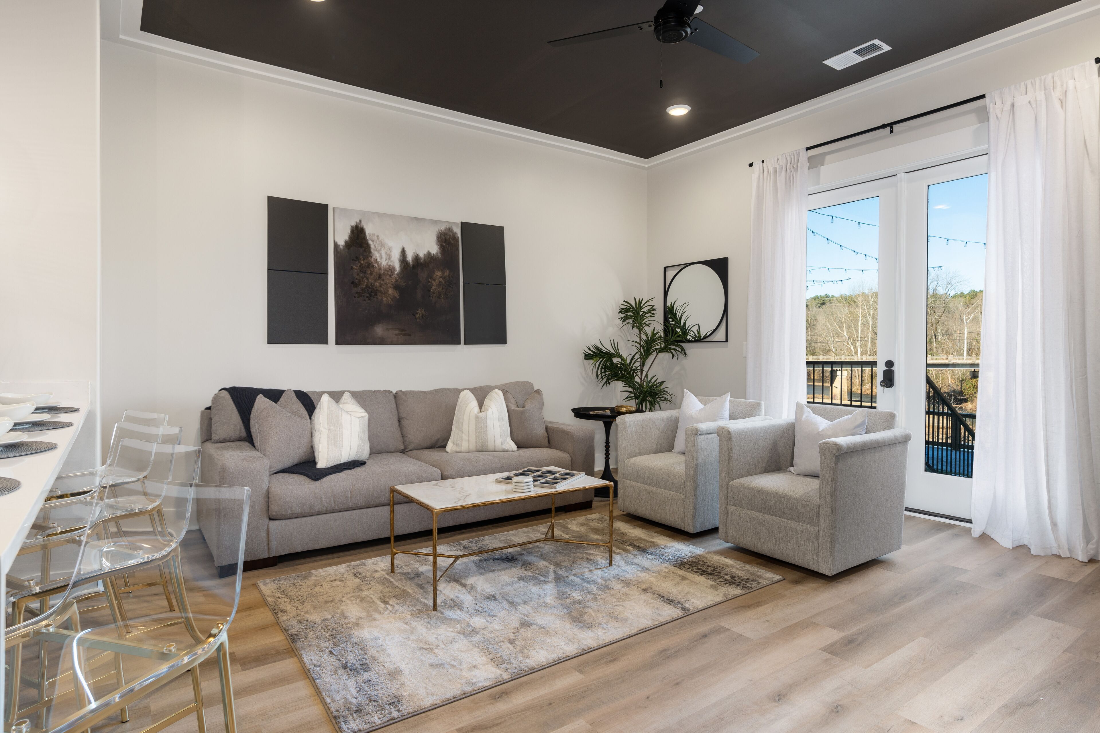 A modern living room with a sofa, armchairs, a coffee table, and a dining area with clear chairs.