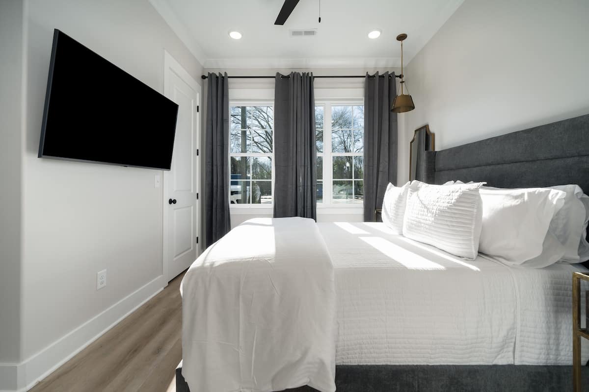 Une chambre à coucher avec un grand lit, un téléviseur à écran plat fixé au mur et une fenêtre avec des rideaux.