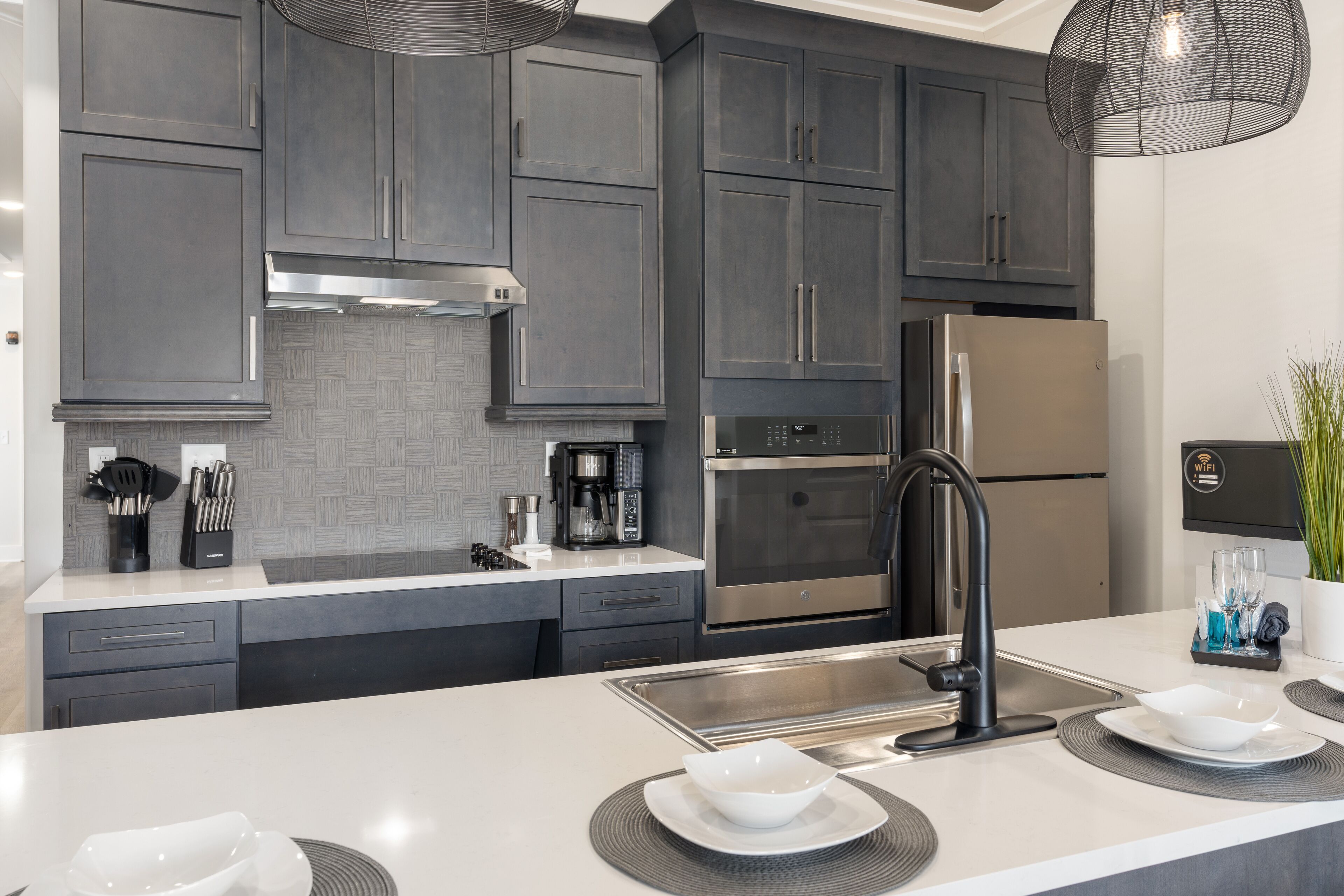 A modern kitchen with dark grey cabinets, stainless steel appliances, and a white countertop.