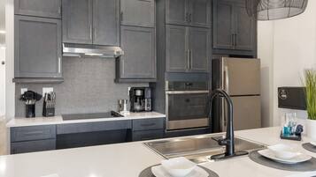 A modern kitchen with dark grey cabinets, stainless steel appliances, and a white countertop.