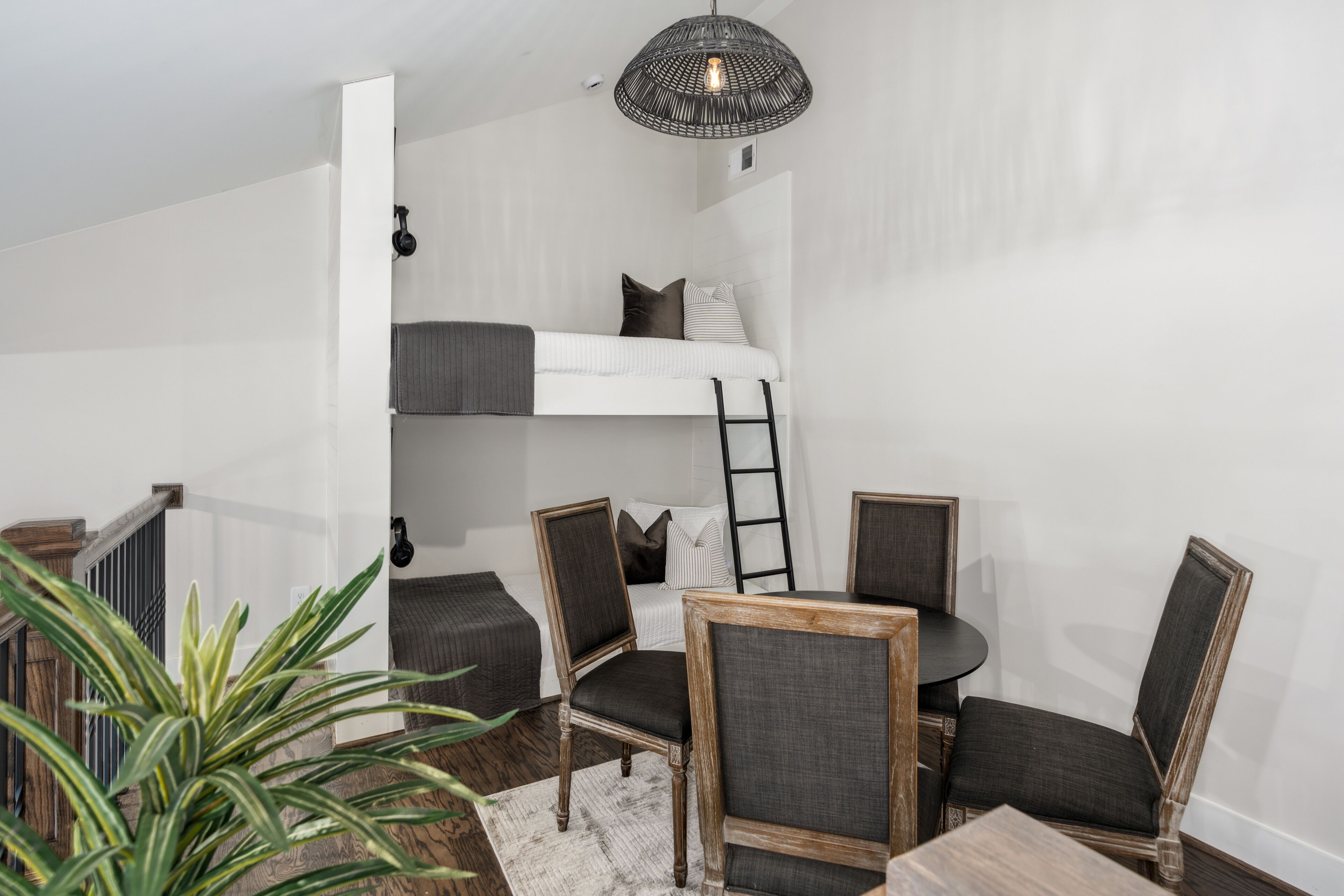 A compact room with a bunk bed, a dining table with chairs, and a hanging light fixture.