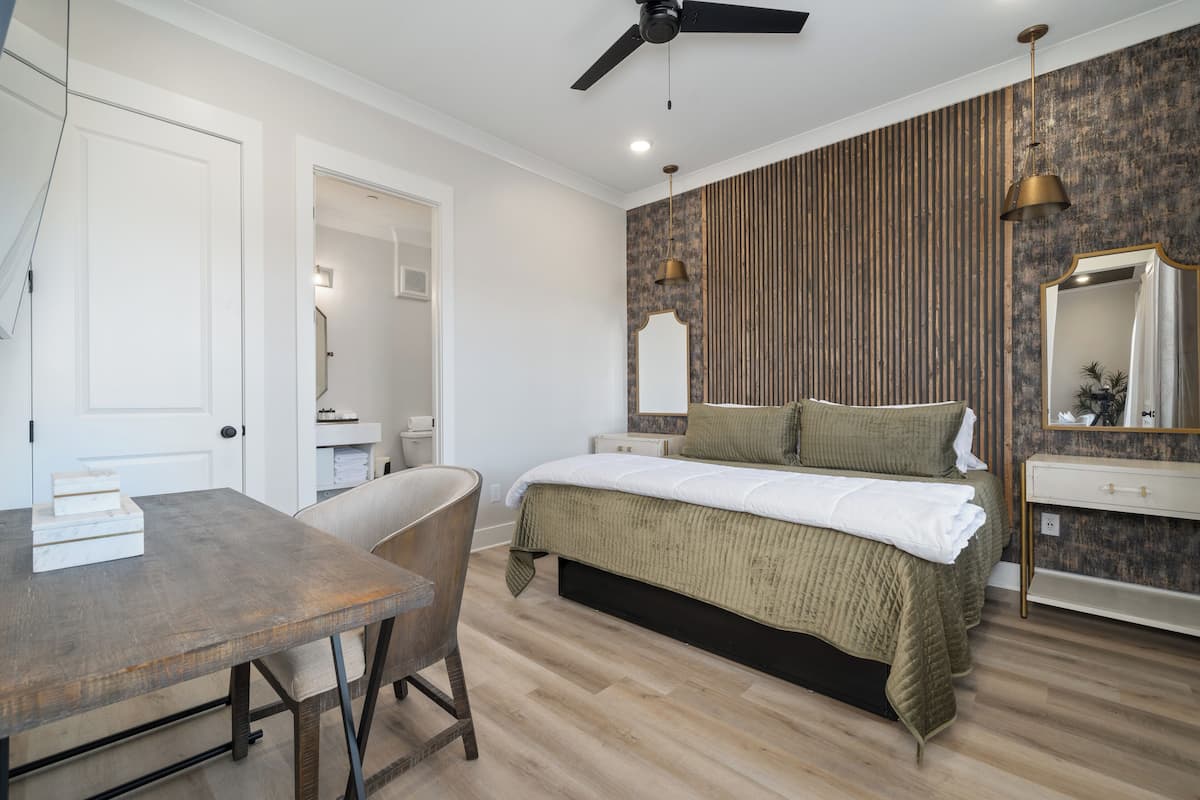 Une chambre à coucher avec un lit, un bureau et une chaise. On y trouve un ventilateur de plafond et un luminaire fixé au mur.