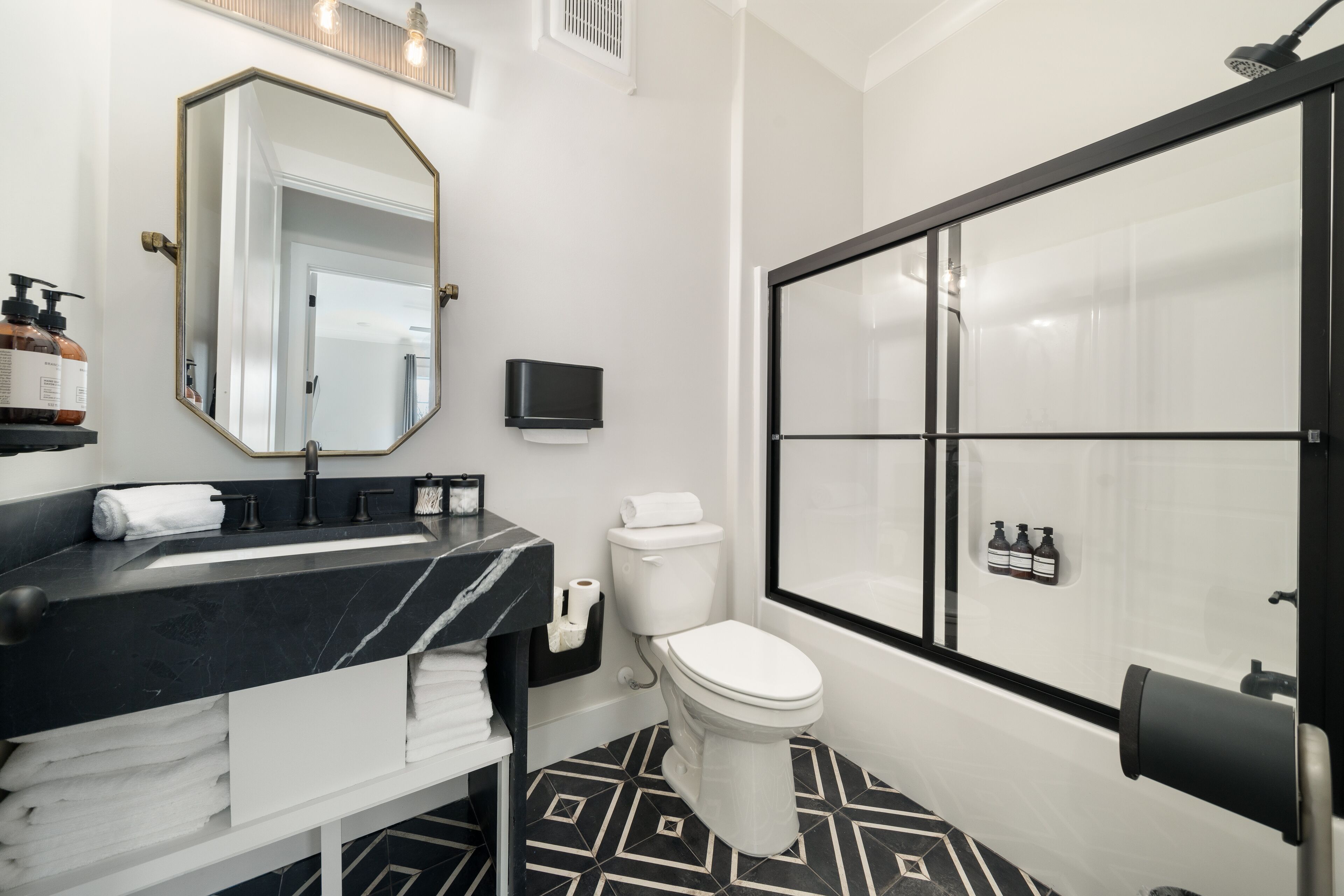 Une salle de bain moderne avec un sol carrelé en noir et blanc, un lavabo en marbre noir, des toilettes blanches et une douche à l’italienne en verre.
