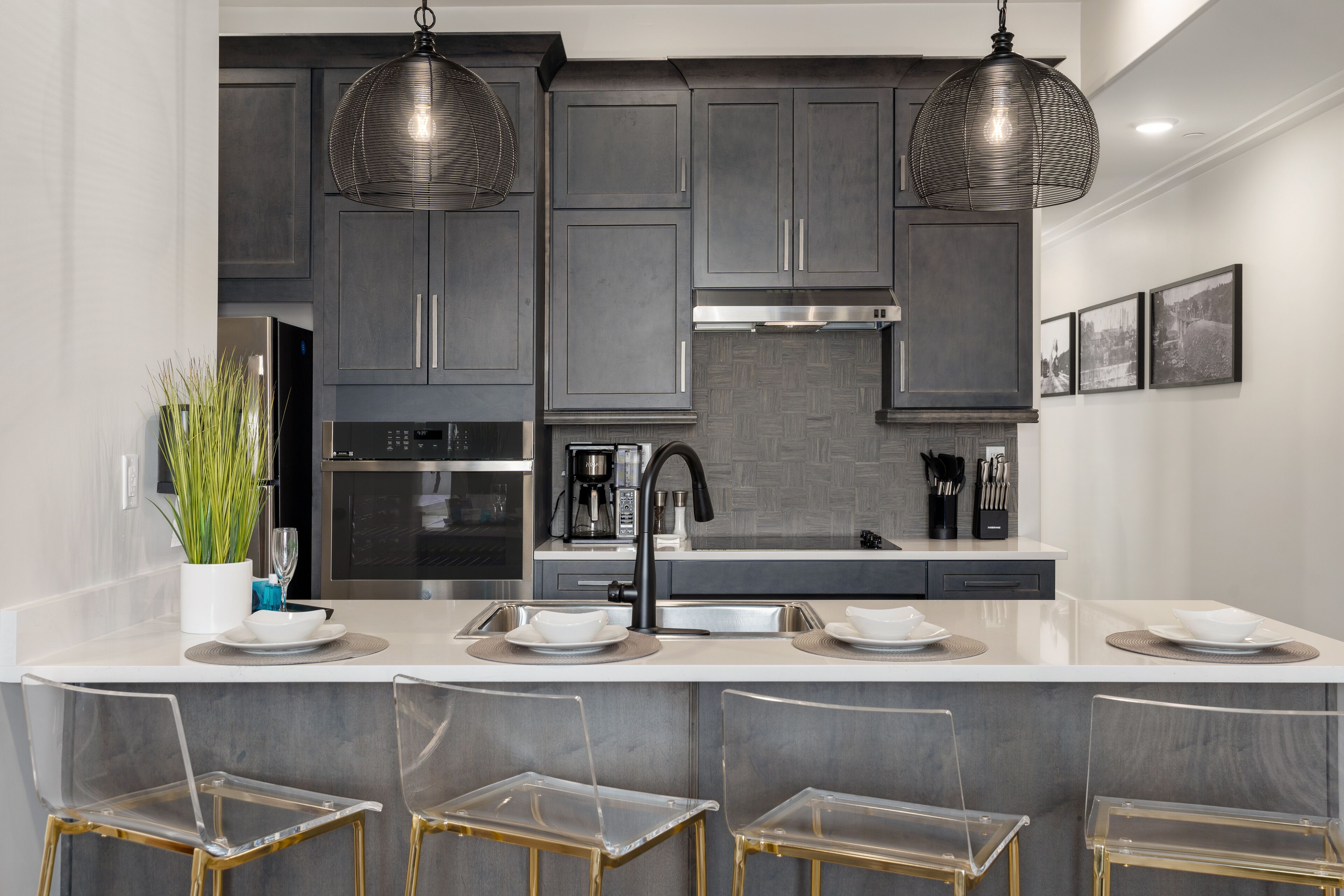 Una cocina moderna con armarios grises oscuros, electrodomésticos de acero inoxidable y una isla central con taburetes de bar.
