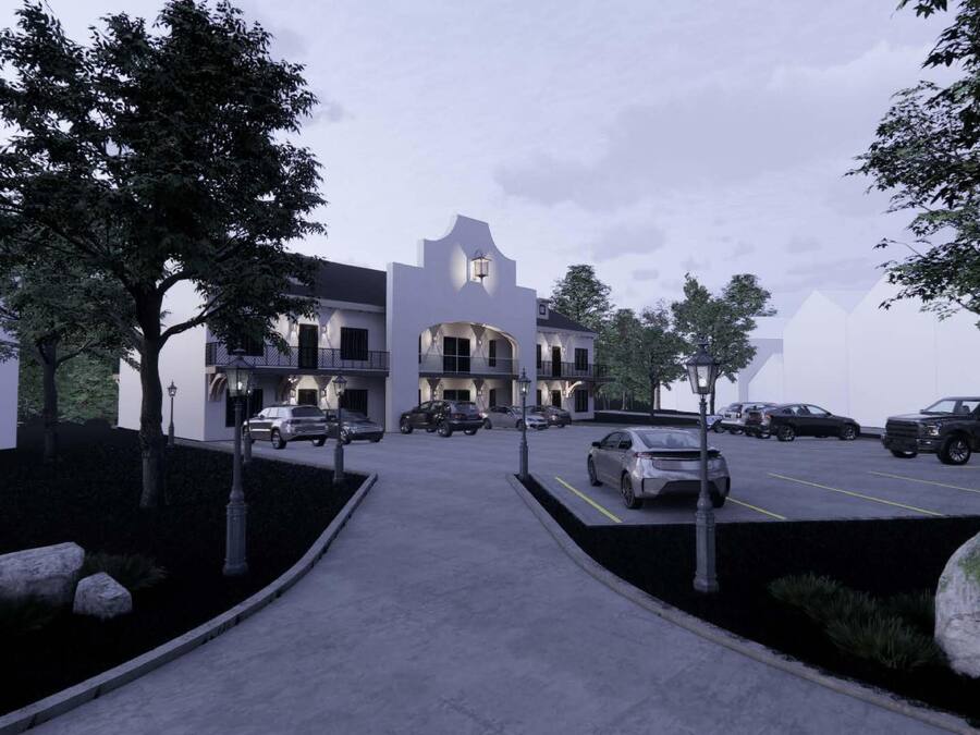 A two-story building with a central courtyard, surrounded by trees and a parking lot with several cars.