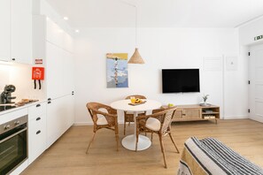 Et moderne køkken med hvide skabe, et spisebord med fletstole, en hængende lampe og et fladskærms-TV monteret på væggen.