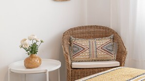A room with a bed, a wicker chair, a small table with a vase of flowers, and two wall-mounted mirrors. - Estrelas da Praia - Stylish and Cozy Apartment (Peniche)