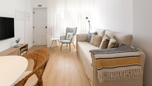 A modern living room with a sofa, a chair, a table, and a television. - Estrelas da Praia - Stylish and Cozy Apartment (Peniche)