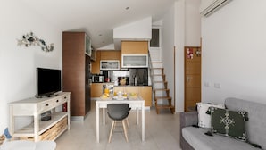 Un espace de vie compact comprenant un coin cuisine, un coin repas, un canapé et un téléviseur.