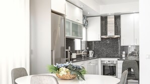Une cuisine moderne avec des meubles blancs, un plan de travail en granit et un coin repas comprenant une table blanche et des chaises grises.
