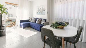 Un salon moderne avec un canapé bleu, une table à manger et des chaises, ainsi qu’une grande fenêtre ornée de rideaux légers.