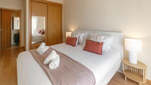 Una cama bien hecha con un edredón estampado, dos almohadas y toallas enrolladas sobre un cubrecolchón blanco.