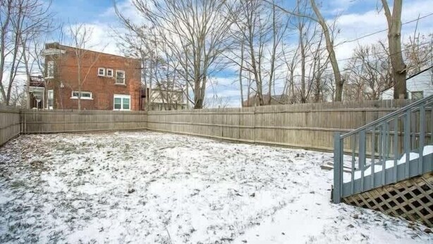 A backyard with a wooden fence, a brick building, and leafless trees.
