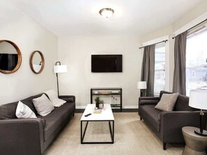 Ett modernt vardagsrum med två soffor, ett soffbord, en tv och ett fönster med gardiner.