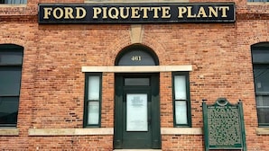 A brick building with a sign reading 'FORD PIQUETTE PLANT' and a plaque with historical information.