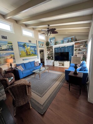 A living room with a blue sofa, wicker chairs, a glass coffee table, and artwork on the walls. - The Mangrove Hideaway 3 bed 2 bath (Cocoa Beach)