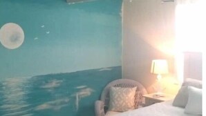 Camera da letto con un murale raffigurante l'oceano, un letto, una sedia e un comodino con una lampada.