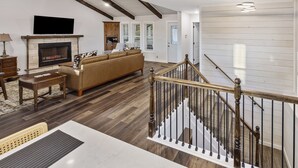 A spacious living room with a fireplace, a large sofa, and a staircase with a wooden railing. - Eagle Ridge - Ridge Road Scenic Cabins - Brimstone Recreation and Big South Fork (Robbins)