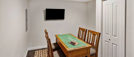 Une pièce comprenant une table de billard, quatre chaises, un téléviseur fixé au mur et une porte.