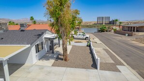 A residential area with a white house, a driveway, a parked white pickup truck, and a body of water in the background. -  Stepping Stones  away from the Colorado River. (Bullhead City)