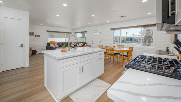 A modern kitchen with white cabinetry, a central island, and a dining area with wooden chairs and a table. -  Stepping Stones  away from the Colorado River. (Bullhead City)