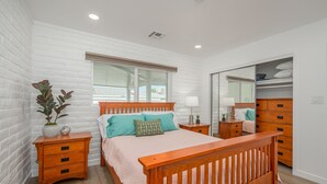 A bedroom with a wooden bed, white brick walls, a window, a bedside table, a nightstand, and a wardrobe. -  Stepping Stones  away from the Colorado River. (Bullhead City)