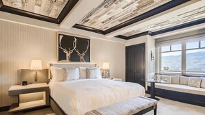 Habitación de hotel con una cama grande, un banco, una mesita de noche, una obra de arte en la pared, una ventana con vistas y un techo con diseño que imita la madera.
