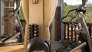 Un gimnasio con cintas de correr y equipo de ejercicio, una luz instalada en la pared, y vistas a un paisaje montañoso a través de amplias ventanas.