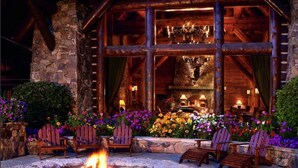A log cabin with a stone fireplace, outdoor seating, and a fire pit.