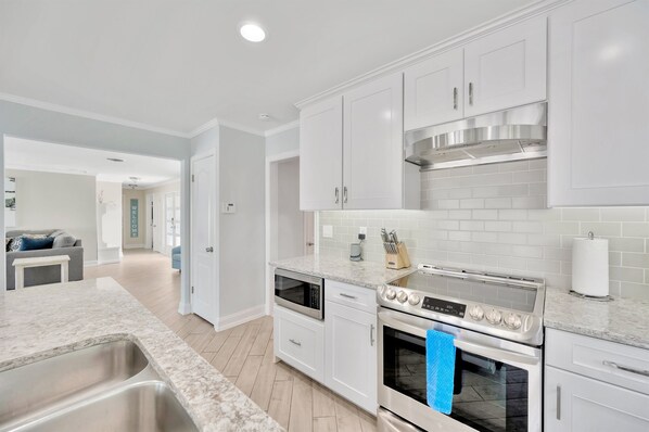 A modern kitchen with white cabinets, stainless steel appliances, and a marble countertop. - Ocean View | Heated Pool | 3 Bedroom | Golf Cart (indian rocks beach)