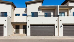 A modern multi-story residential building with a flat roof, large garage doors, and a clear blue sky.