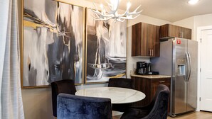 A modern kitchen with a stainless steel refrigerator, a round marble table, and dark velvet chairs.