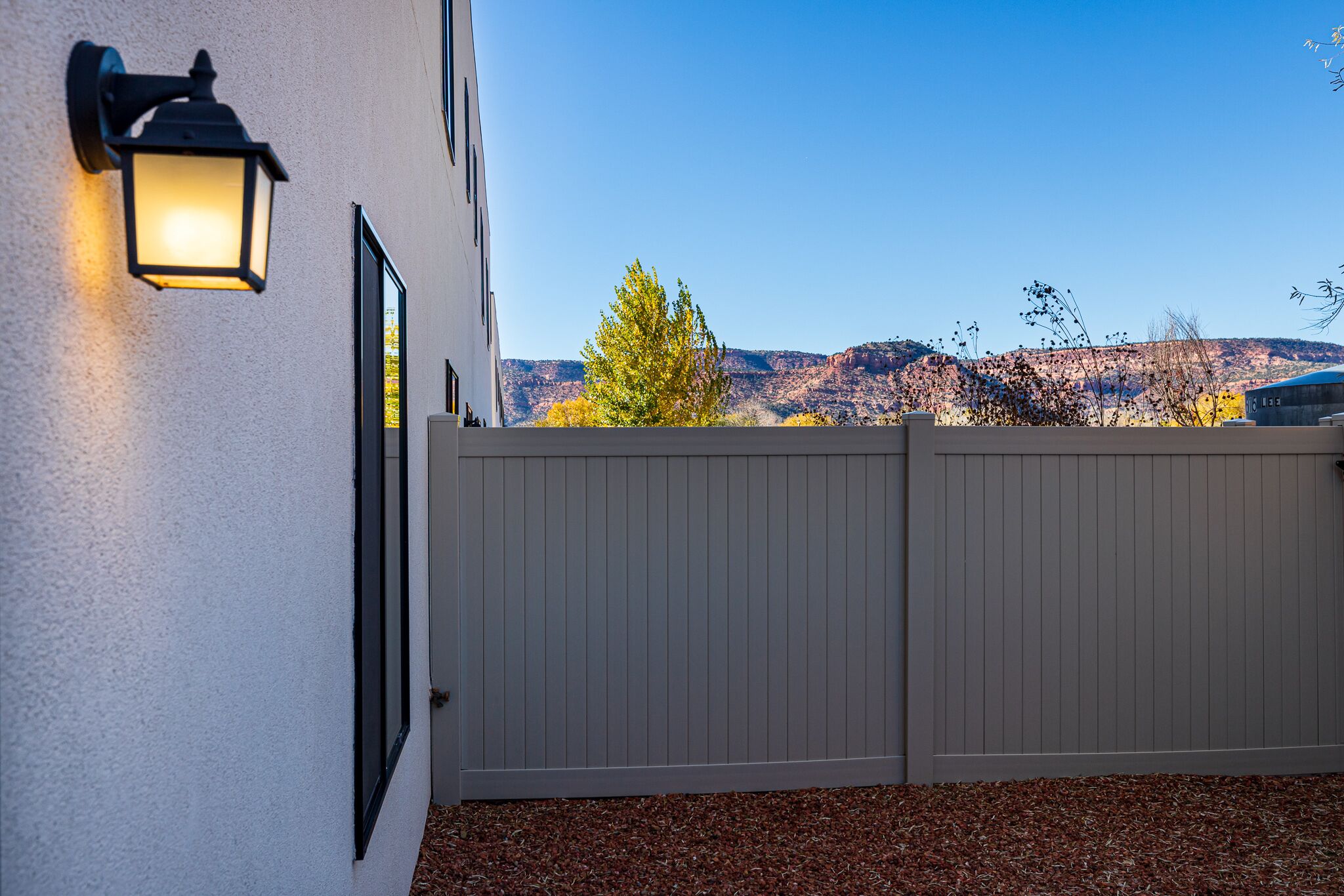 A gated entrance with a light fixture on the wall, a wooden fence, and a view of a mountain range.