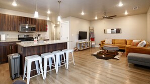 A modern kitchen with a central island, bar stools, a microwave, and a TV in the living area.