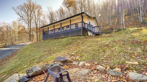 Une cabane dotée d’un porche, entourée d’une zone boisée où les feuilles mortes jonchent le sol.