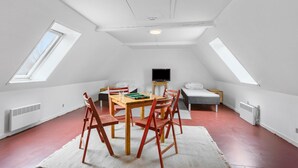 Une pièce mansardée spacieuse avec un plafond en pente, des fenêtres de toit, une table à manger avec des chaises, un téléviseur et un lit.