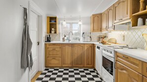 Une cuisine compacte avec des meubles en bois, un carrelage noir et blanc, un four encastré et une fenêtre au-dessus de l’évier.