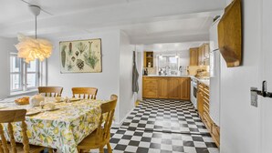 Une cuisine avec des meubles en bois, un carrelage à motifs et un coin repas avec une table dressée pour quatre personnes.