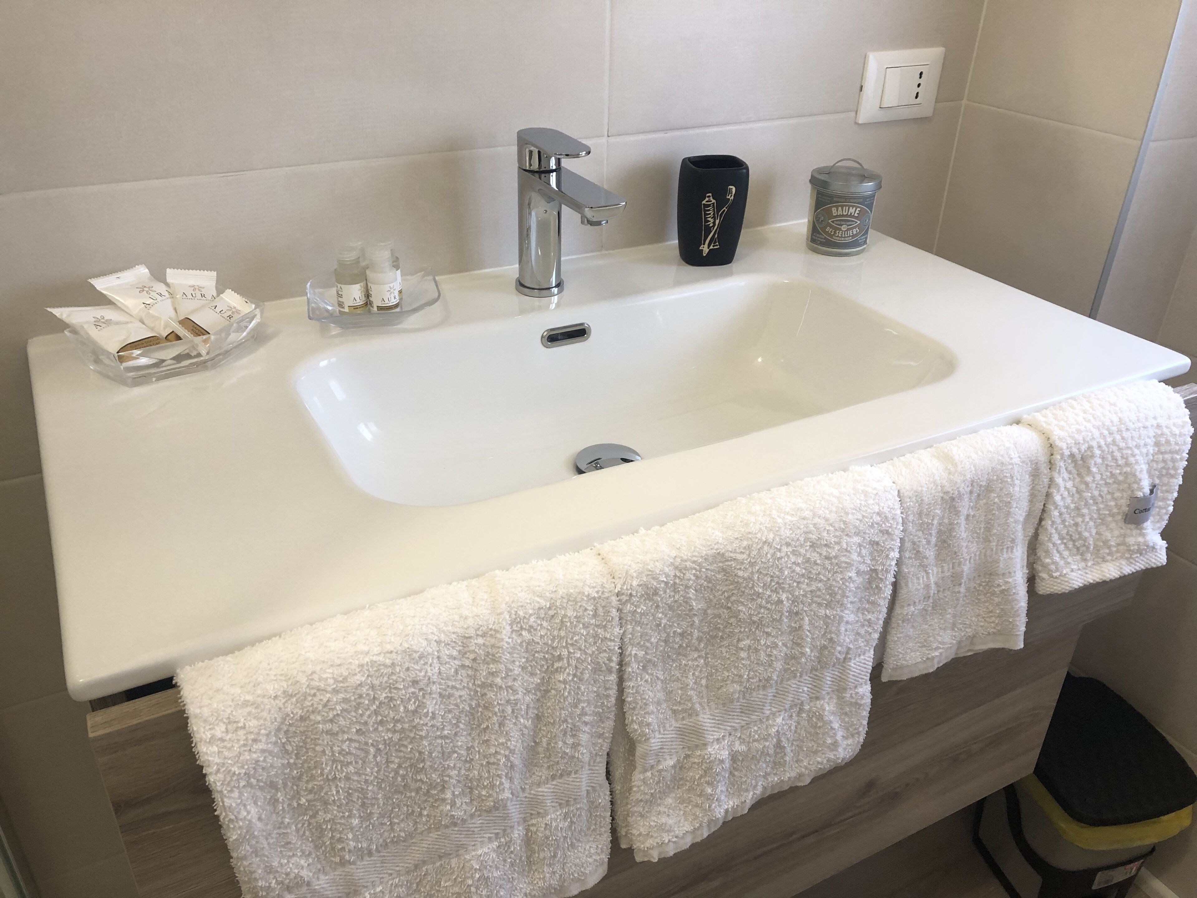 Un baño con lavamanos blanco, un espejo y artículos de aseo, incluyendo un portalápices para cepillos de dientes y un jabonero.